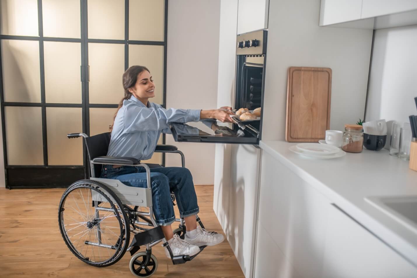 A person in a wheelchair opening an oven Description automatically generated