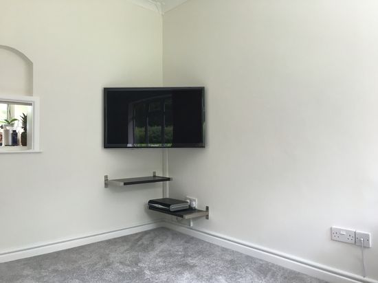 A TV placed in the corner of a room with a shelf nearby, creating a compact and organized entertainment setup