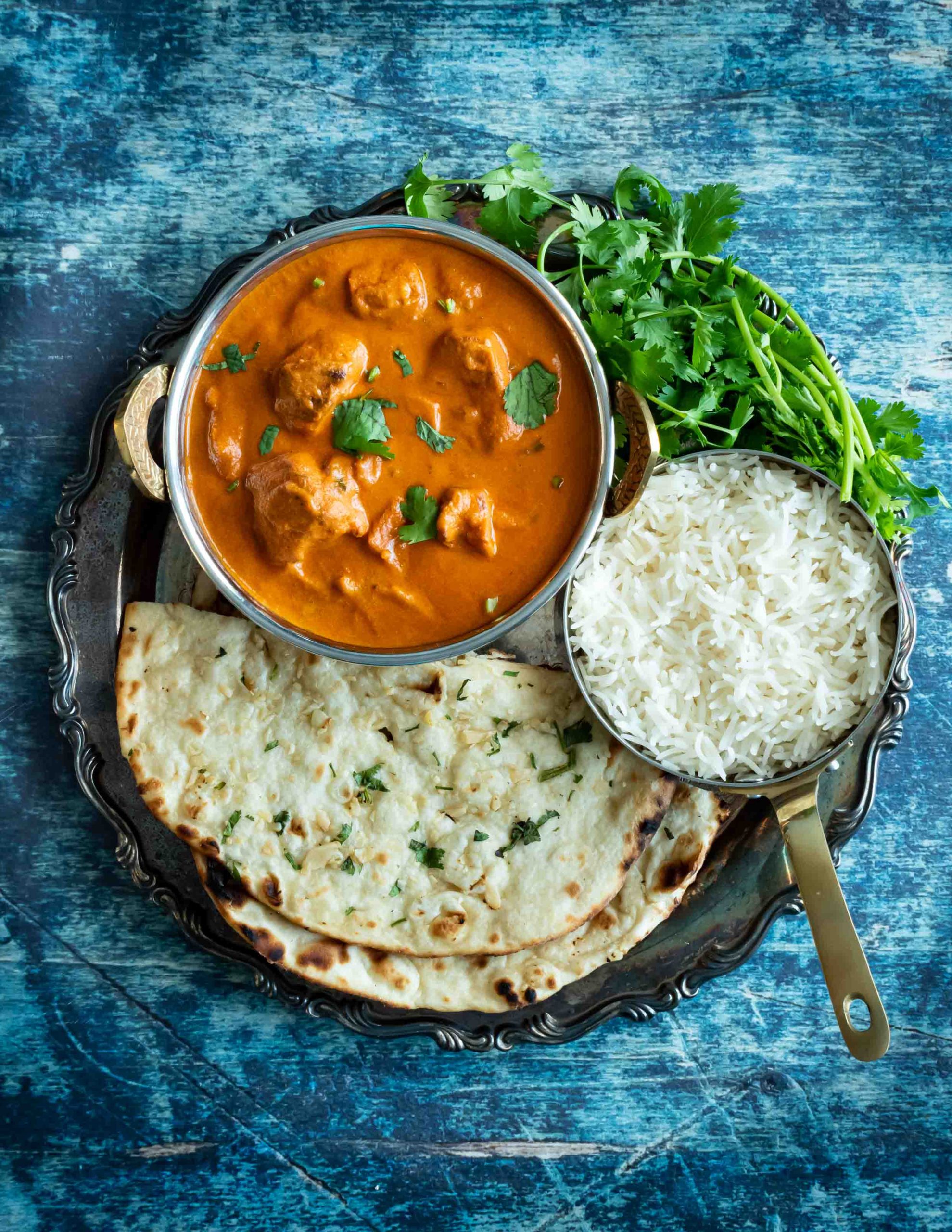 Indian chicken tikka masala curry with naan bread on blue table