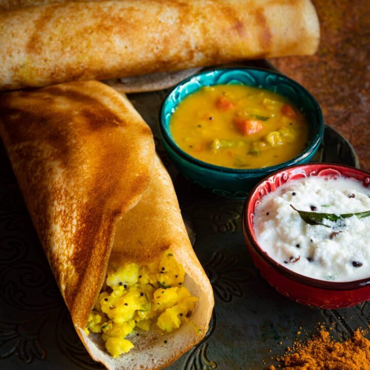 A plate with two Masala Dosa and a bowl of sauce