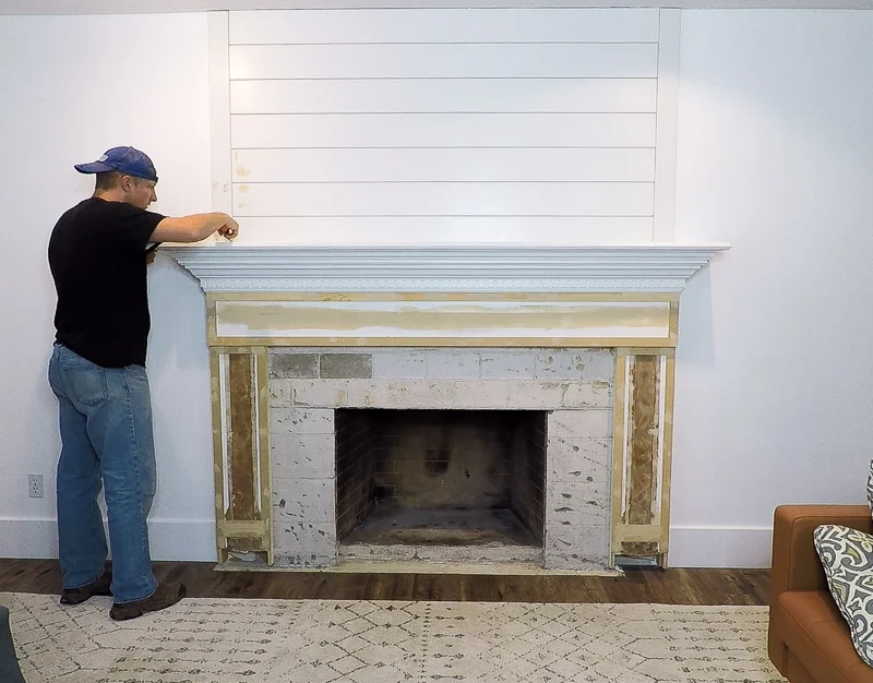 A man installing a fireplace in a living room, removing the old mantel.