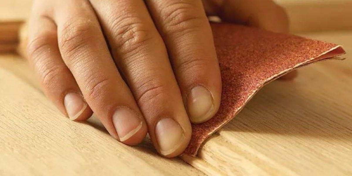 A person sanding wood with a sanding pad to smooth its surface