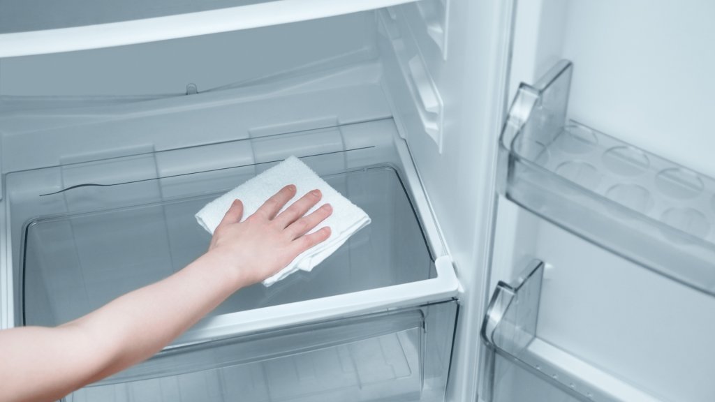 Interior of an open refrigerator being wiped down by a person, ensuring cleanliness and hygiene