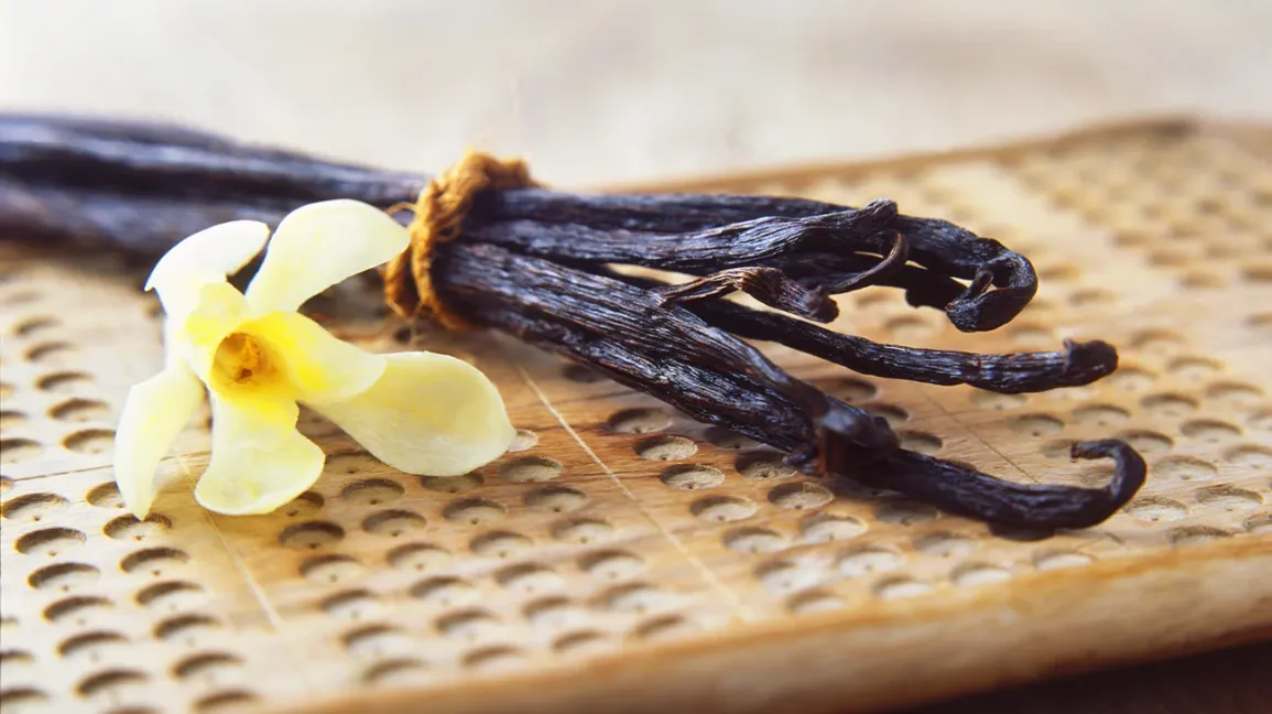 Vanilla beans and a flower on a wooden surface