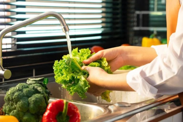 A person washing lettuce in a kitchen sink.