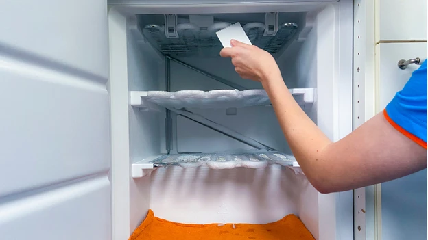 A person cleaning an open refrigerator, removing ice buildup during the defrosting process