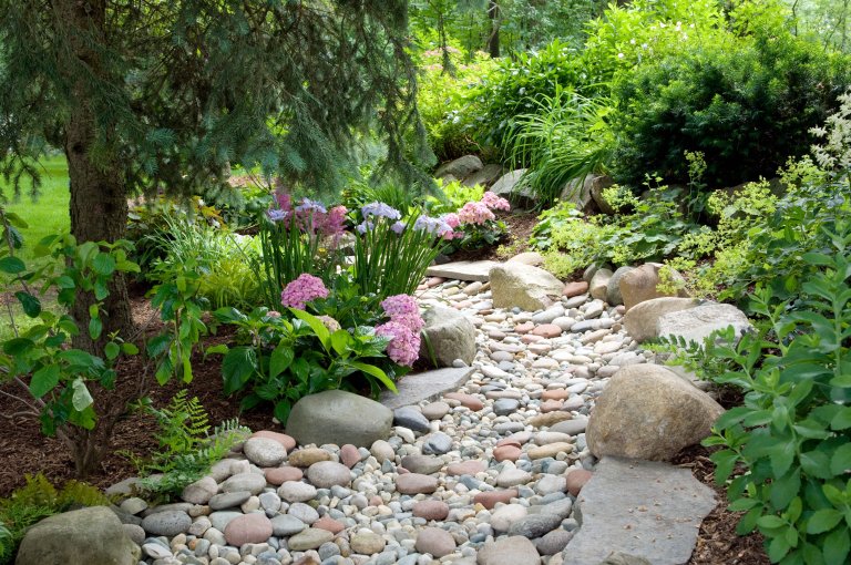 A gravel path leading to a house with a moose statue. Consider using landscape fabric on dry creek bed